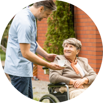 A young man passing a cup of tea to an elderly woman in a wheelchair.