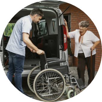 A young man loading an elderly woman's wheelchair into a vehicle as she looks on.