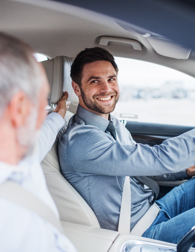 A young man in the driver's seat, smiling at his eldery passenger.